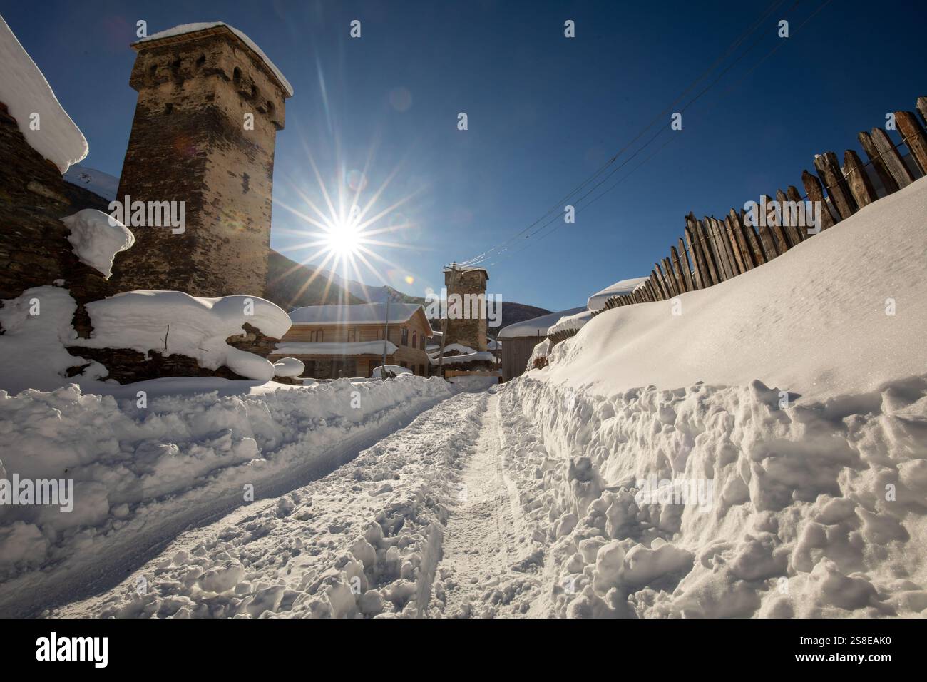 Eine malerische Winterszene eines schneebedeckten Dorfes mit alten Steintürmen in Georgien die helle Sonne scheint am klaren blauen Himmel und wirft lange Schatten Stockfoto