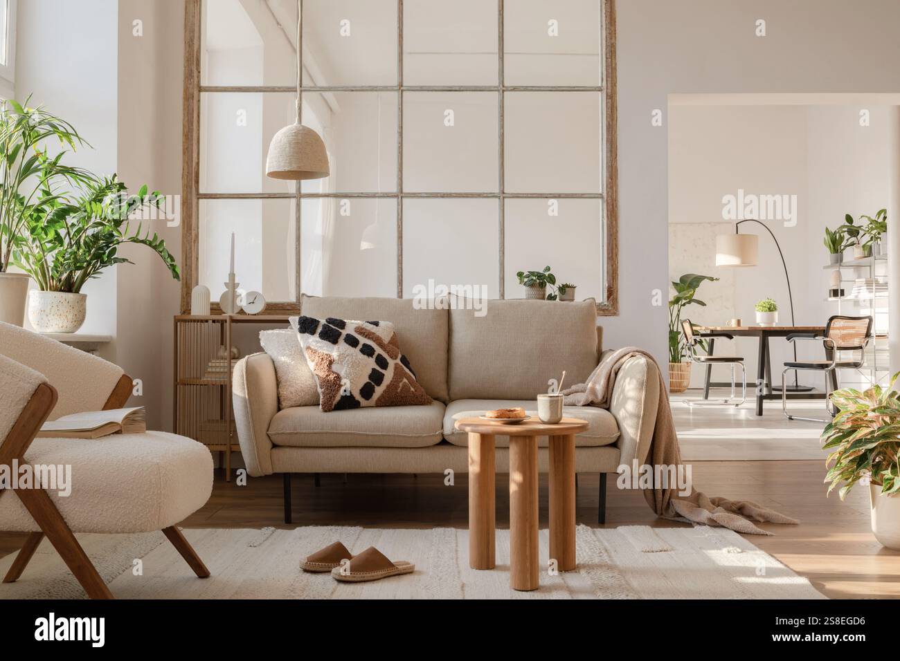 Elegante Inneneinrichtung im Wohnzimmer mit beigefarbenem, modernem Sofa, Beistelltisch und kreativen Accessoires. Vorlage. Kopierbereich. Speisesaal im Hintergrund. Stockfoto