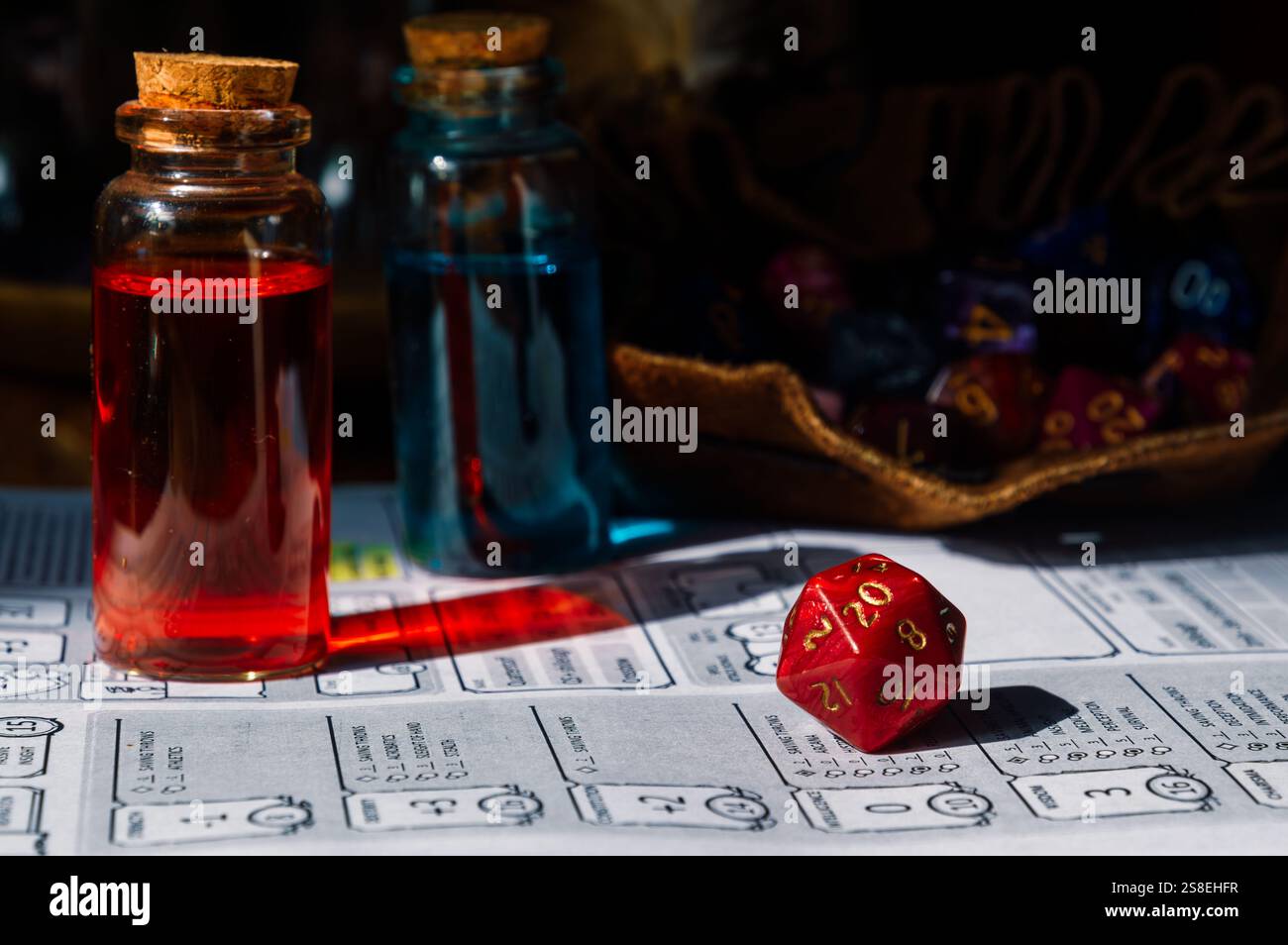 Eine leuchtend rote D20-Würfel, Tränkflaschen und ein Zeichenblatt für ein Rollenspiel auf der Tischplatte. Stockfoto