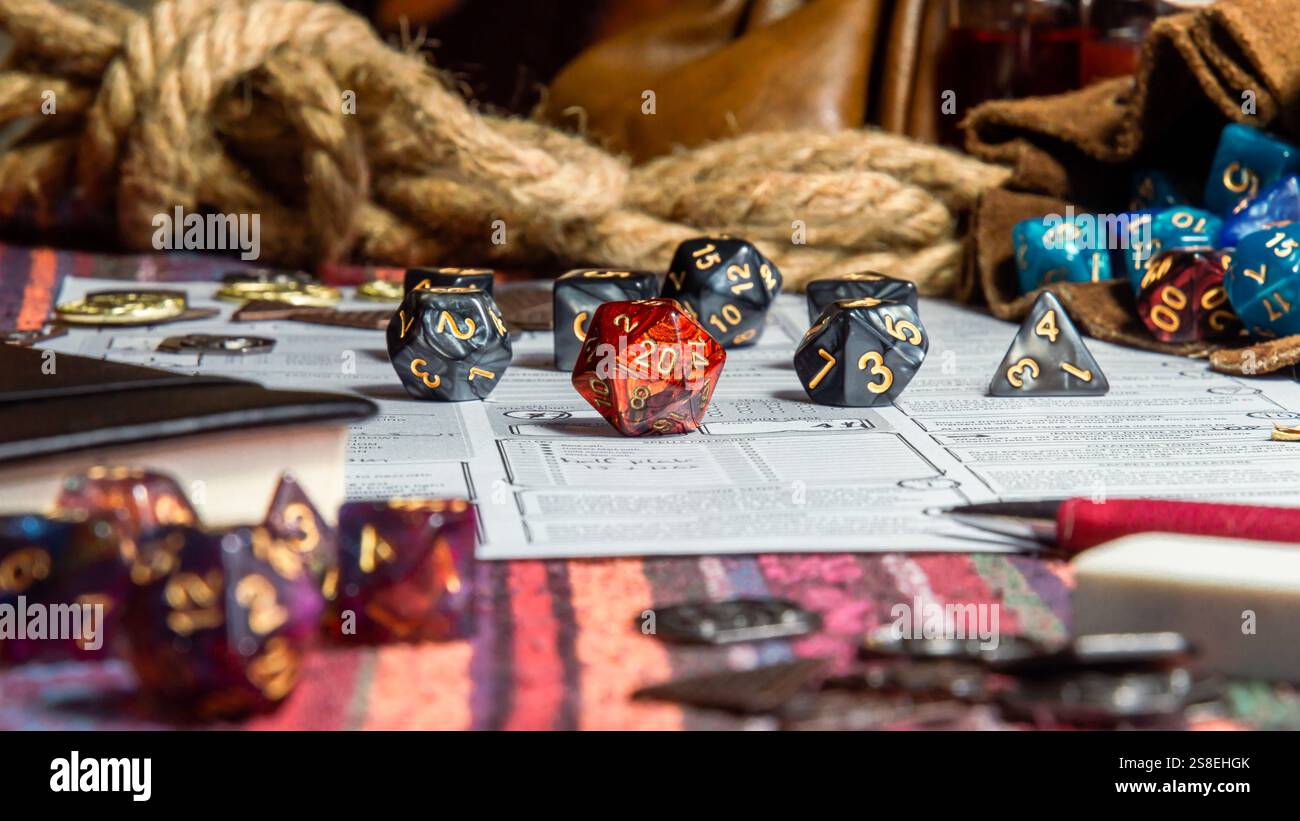 Lebendige RPG-Würfel, einschließlich eines roten D20, angeordnet auf Charakterbögen, umgeben von Spielerquips und Zubehör. Stockfoto