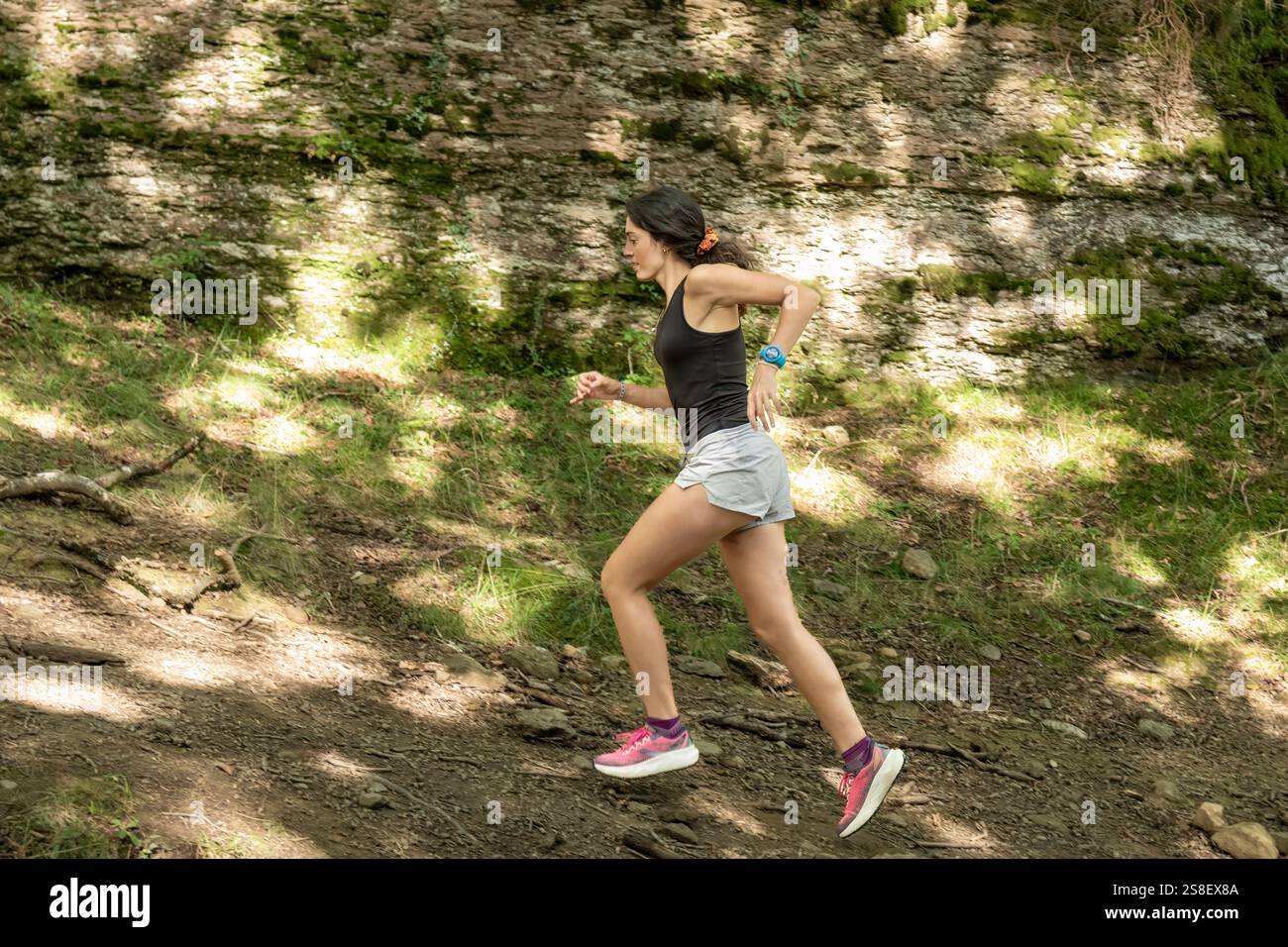 Frau, die auf einem Waldweg bergauf läuft, in sportlichem Outfit, zeigt Fitness, Entschlossenheit und Outdoor-Aktivitäten in einer natürlichen Umgebung Stockfoto