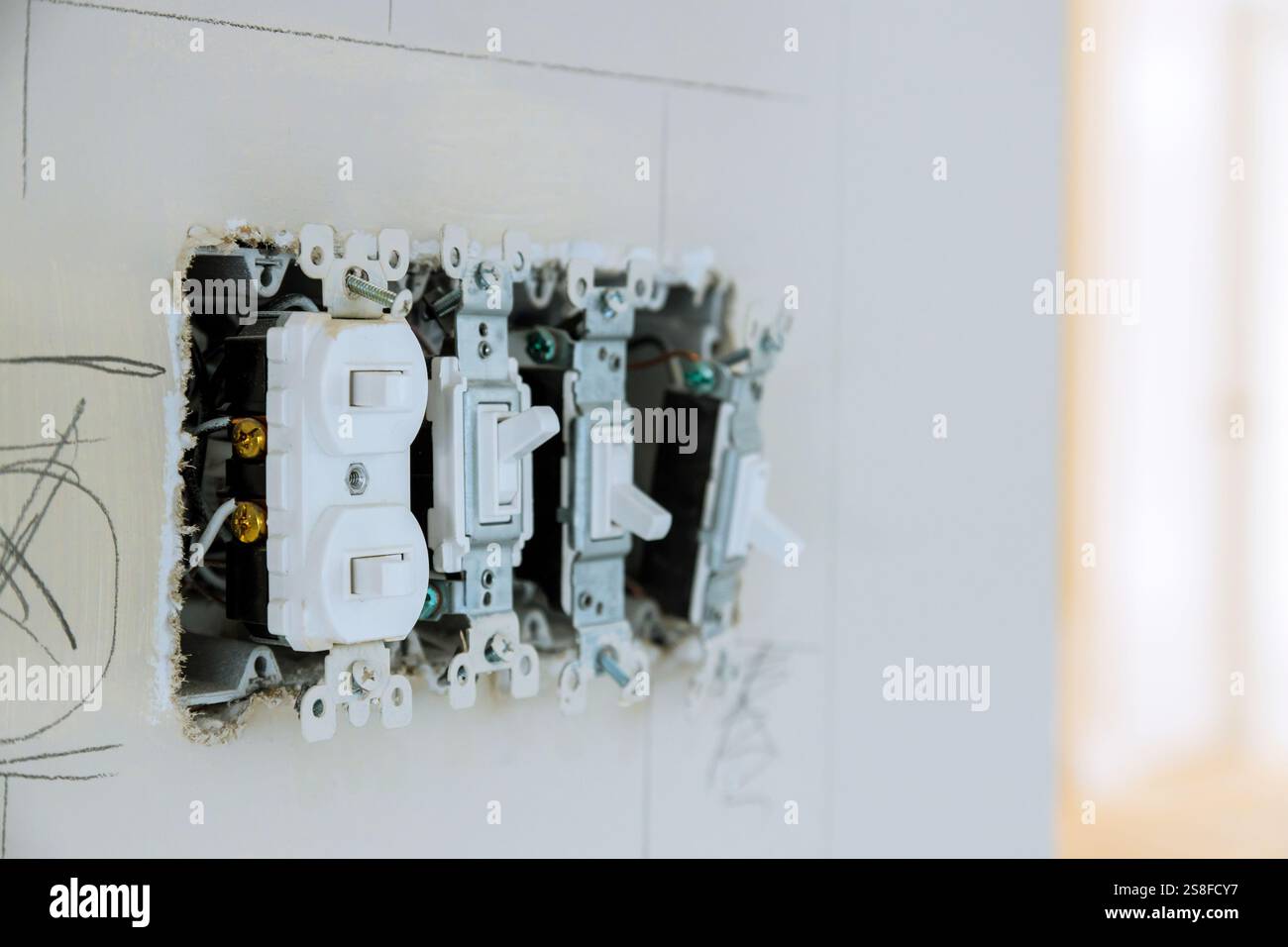 Elektriker arbeitet an mehreren Schaltern, Steckdosen in einem lichtdurchfluteten Raum des im Bau befindlichen neuen Hauses. Stockfoto