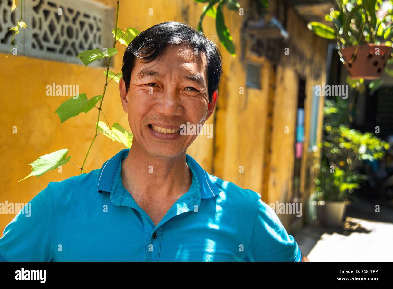Ein glücklicher vietnamesischer Mann lächelt vor seinem gelb bemalten Haus in hoi an vietnam Stockfoto