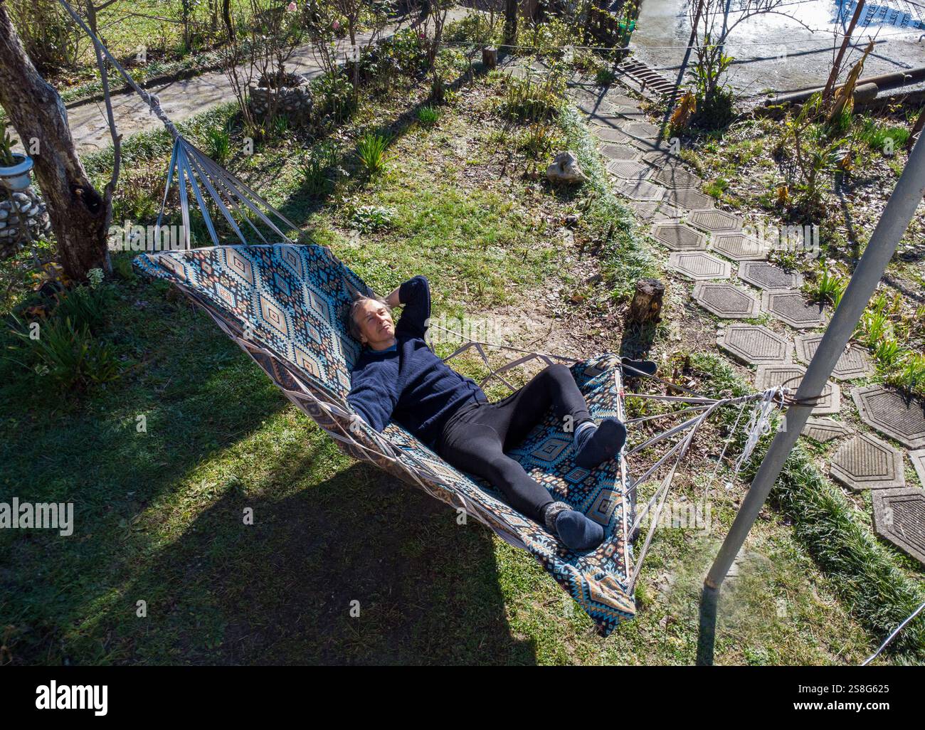 Glücklicher chinesischer Ethnicity Mann in seinen 60ern genießt die Sonne (entspannend) in Florida im Winter in einer Hängematte (Hinterhof des Hauses), grünem Gras und Persimmon ( Stockfoto