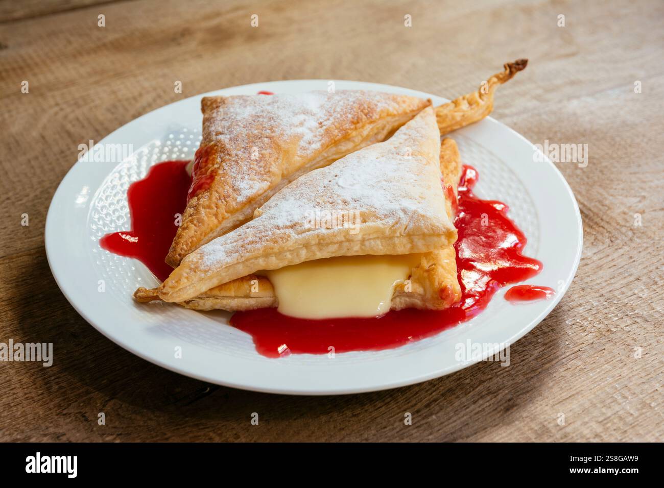 Veganer Vanillepudding und Blätterteig auf einem Teller mit roter Johannisbeersauce. Stockfoto