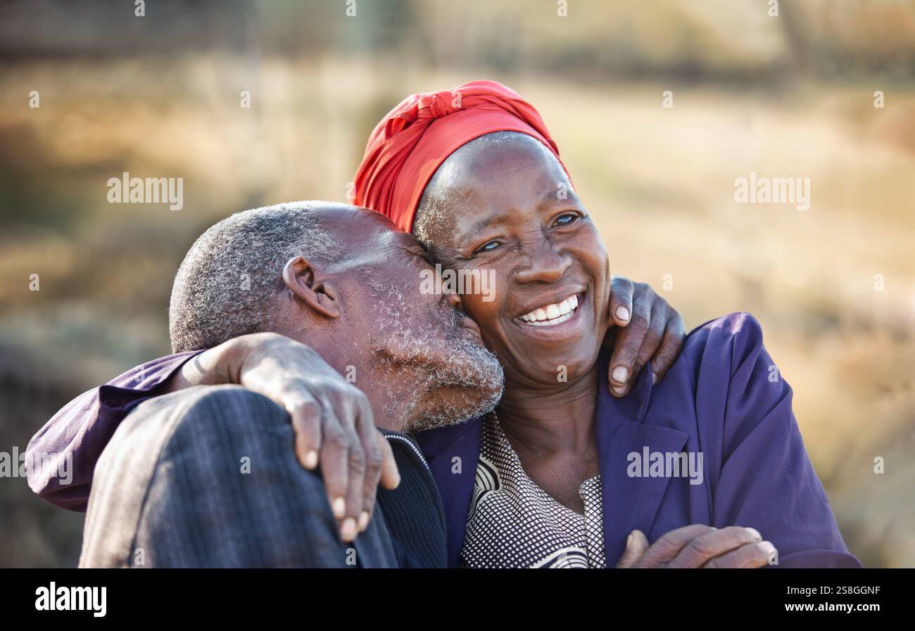 afrikanisches Dorf, küsst ältere afrikanische Paare draußen, umarmt einander glücklich, setzt sich zusammen, ein großes zahnartiges Lächeln glücklich Stockfoto