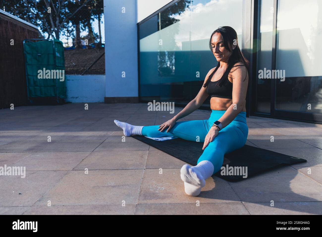 Eine Frau sitzt auf einer Matte und beginnt ihr Workout, fit Lifestyle Stockfoto