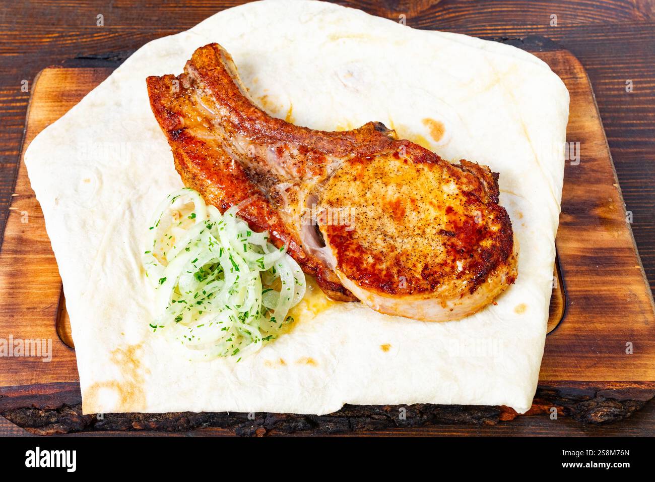 Perfekt gegrillte Rippchen ruhen auf einem warmen Fladenbrot, garniert mit dünn geschnittenen Zwiebeln und Kräutern. Dieses Gericht ist ideal für eine zwanglose Dining-Tour Stockfoto
