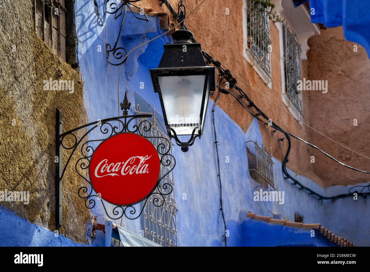 Chefchaouen, Marokko. Vintage Coca Cola Schild mit einer Straßenlampe im Hintergrund auf einer alten Schlauchfassade mit Blick auf eine Gasse in der blauen Stadt Medina. Stockfoto