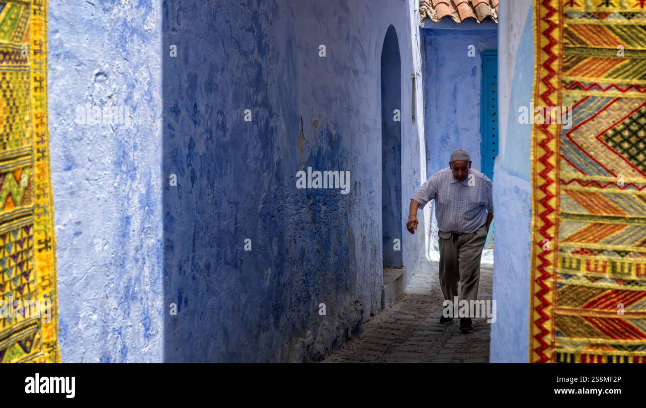Chefchaouen, Marokko. Älterer marokkanischer Mann, der auf einer engen Gasse in der blauen Stadt Medina spaziert. Stockfoto