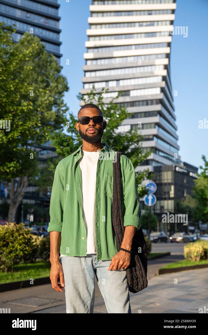 Selbstbewusster afroamerikanischer Mann in Sonnenbrille fokussierte Blicke im Wolkenkratzer-Hintergrund der Stadt. Stockfoto