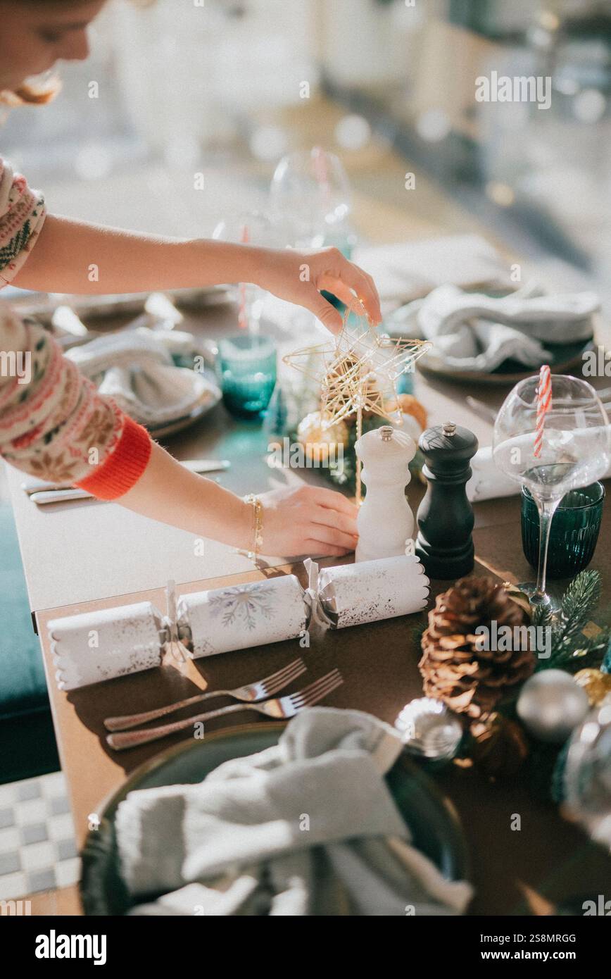 Eine Frau stellt einen Tisch für ein Weihnachtsessen. Sie legt einen Stern auf einen Weihnachtsbaum und fügt ein paar Tannenzapfen auf den Tisch. Die Tabelle Stockfoto