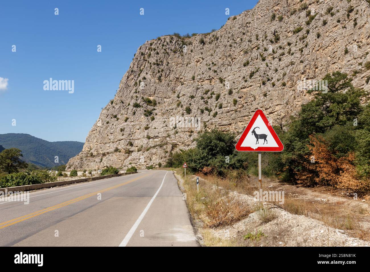 Ein landschaftlich reizvoller Abschnitt der Gorgan-Bojnord-Straße im Golestan-Nationalpark zeigt ein Schild mit Wildtieren vor dem Hintergrund steiler Klippen und Grünflächen. Stockfoto