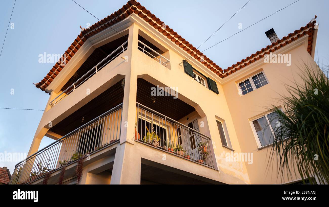Ein modernes Haus im mediterranen Stil mit einer beigefarbenen Fassade, großen Balkonen und einem Dach mit Terrakotta-Fliesen. Das warme Sonnenlicht unterstreicht die architektonische d Stockfoto
