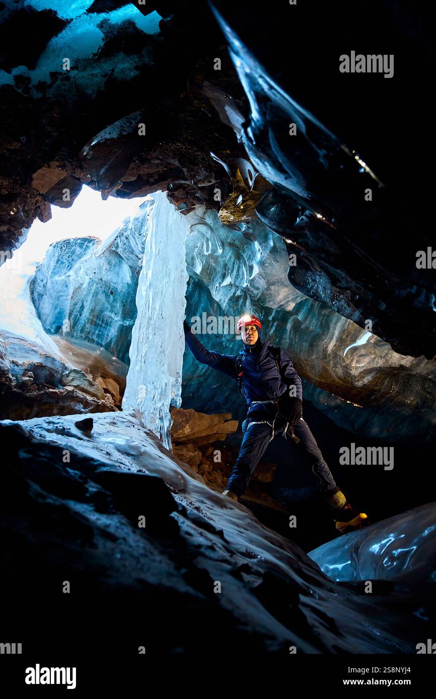 Man klettert in einer gefrorenen Eishöhle mit gefrorenem Wasserfall im Inneren des großen Gletschers mit Eisaxt und rotem Helm in den Winterbergen. Sportbergsteigen A Stockfoto
