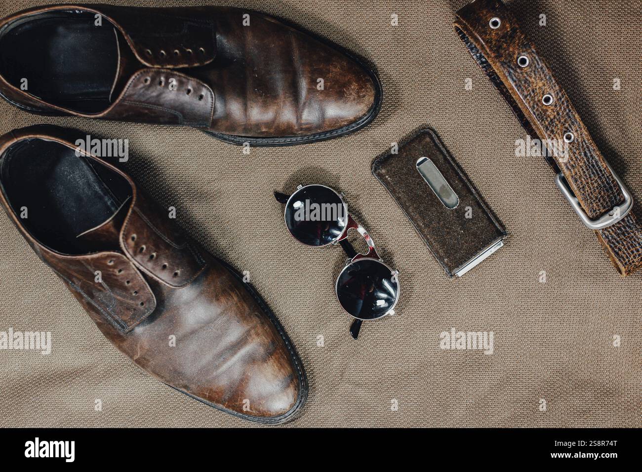 Braune Vintage-Schuhe mit Ledergürtel und Sonnenbrille vor strukturiertem Hintergrund Stockfoto