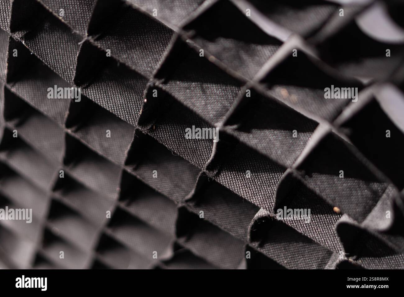 Nahaufnahme eines strukturierten schwarzen Stoffes mit geometrischem Muster, das eine Reihe dreieckiger Formen und Schatten zeigt. Stockfoto