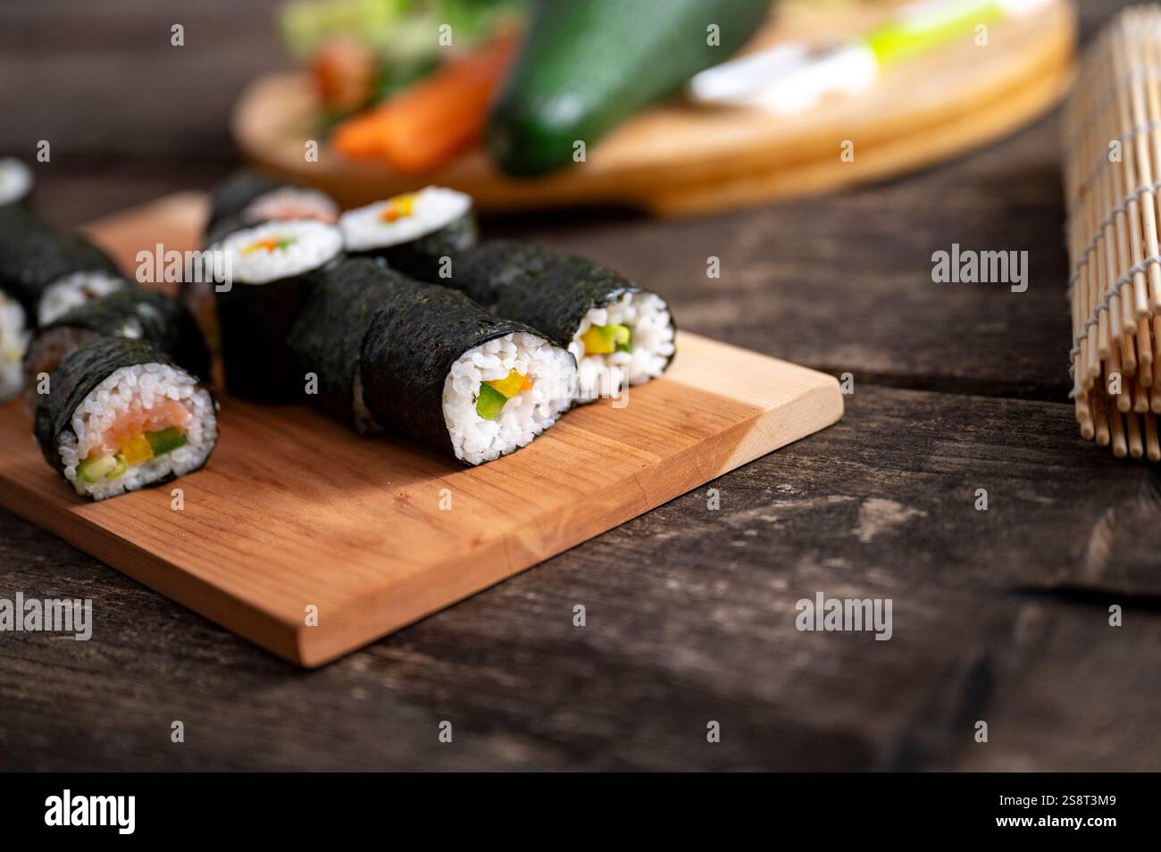 Köstliche hausgemachte japanische Küche Sushi-Brötchen mit Lachsfisch und Gemüse serviert auf einem Holzbrett mit verschwommenem Gemüse im Hintergrund. Stockfoto
