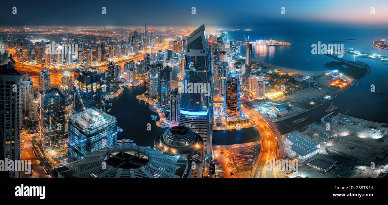 Blick auf die Skyline von Dubai bei Nacht von oben. Mit orange leuchtendem Verkehr auf den Straßen und dunkelblauem Wasser, das mit dem Himmel verschmilzt Stockfoto