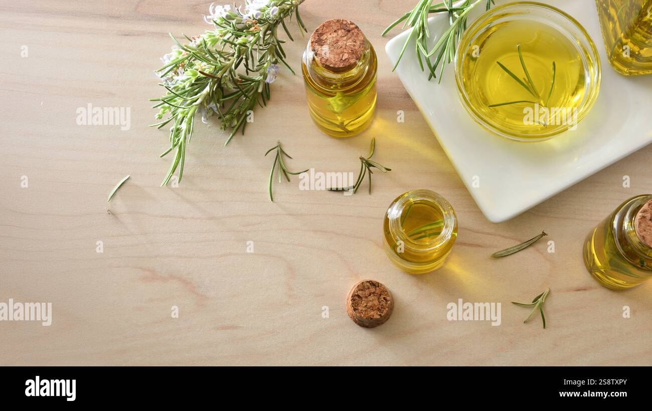 Detail der Gläser mit Rosmarinextrakt und Rosmarinzweigen herum auf einem Holztablett und weißem isolierten Hintergrund. Draufsicht. Stockfoto