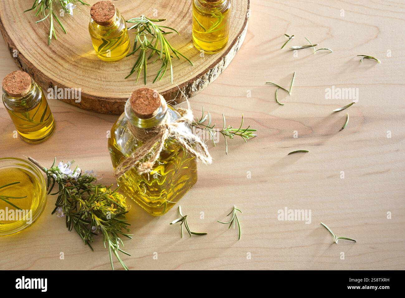 Detailansicht der Behälter mit ätherischem Rosmarinöl auf Holztisch mit Zweigen um sich herum. Draufsicht. Stockfoto