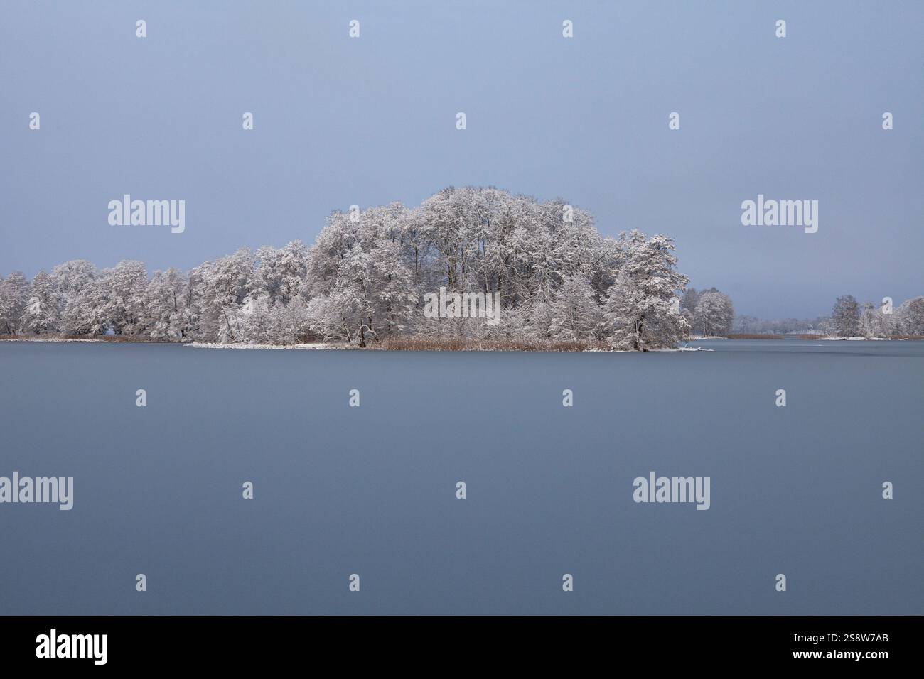 Die Schönheit eines Wintertages zeigt sich in diesem Bild des Galve-Sees in Trakai, Litauen. Die Sonne scheint hell über dem Himmel und strahlt ein warmes Leuchten aus Stockfoto