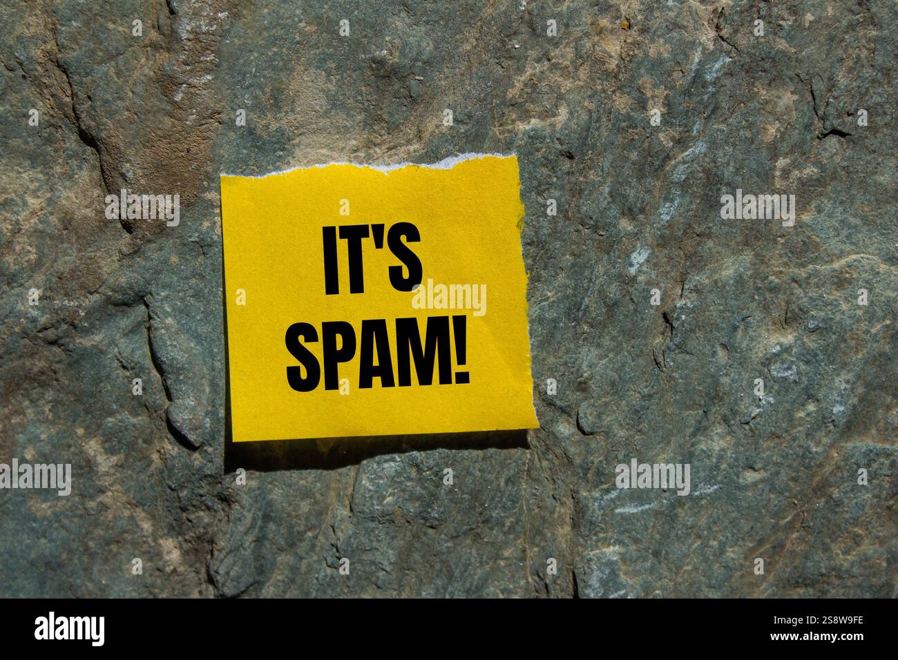 Es ist eine Spam-Nachricht, geschrieben auf zerrissenem gelbem Papierstück mit Steinhintergrund. Konzeptionell ist das Spam-Symbol. Kopierbereich. Stockfoto