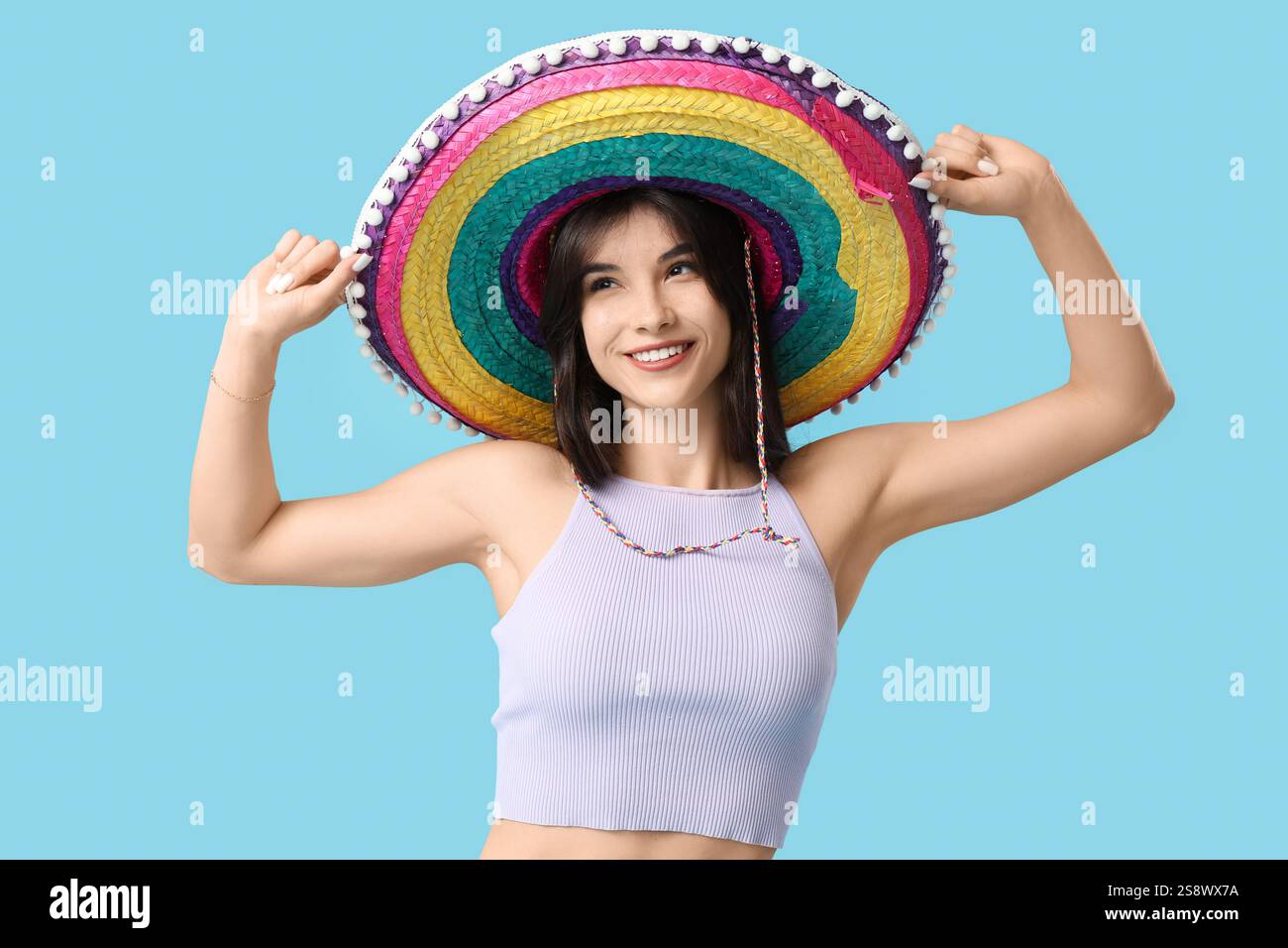 Junge Frau in farbenfrohem Sombrero tanzt auf blauem Hintergrund. Cinco de Mayo-Feier Stockfoto