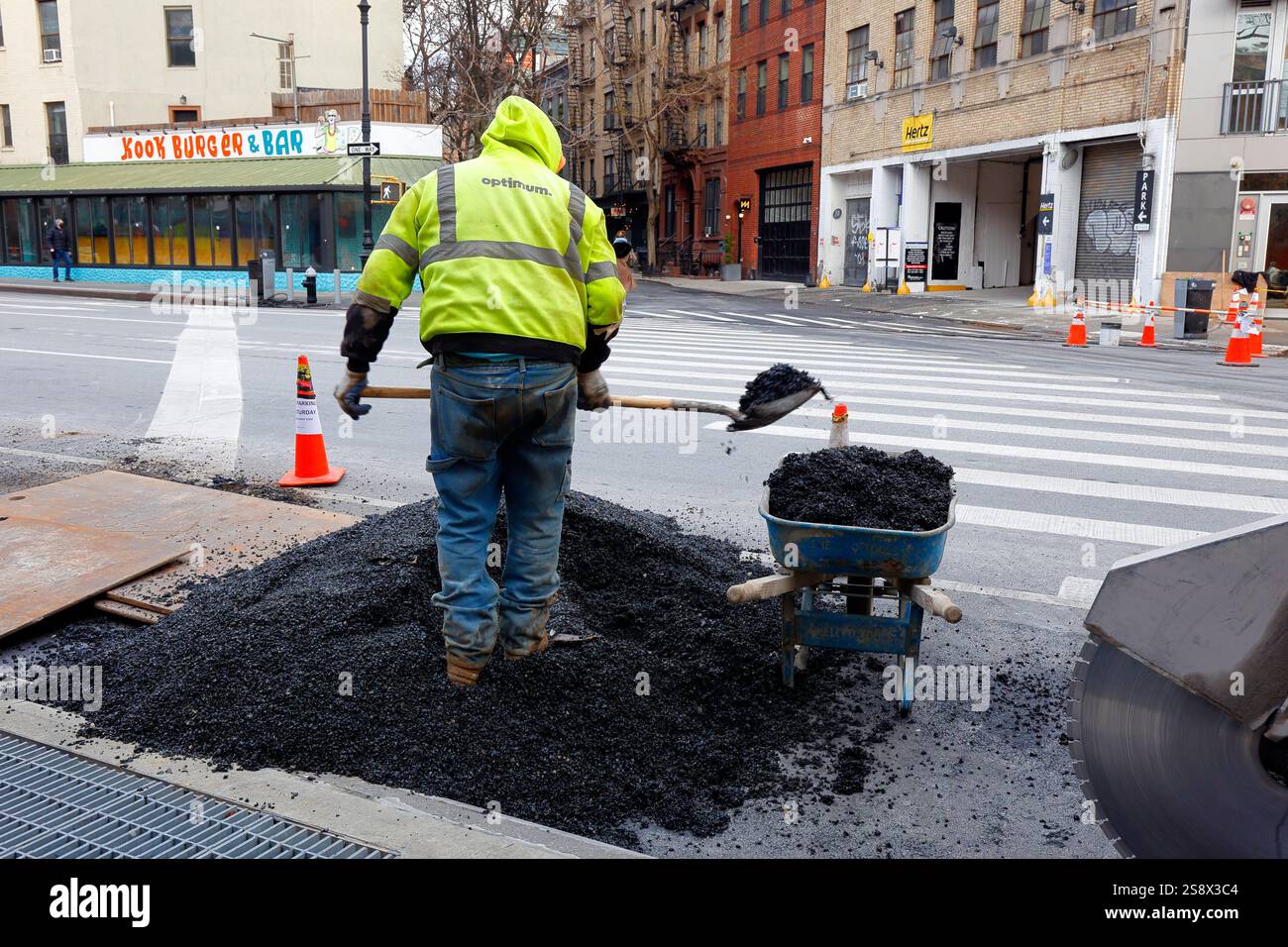 Ein Straßenreparaturarbeiter schaufelt Asphalt in eine Schubkarre an einer Straßenecke in Manhattans West Village, New York City Stockfoto
