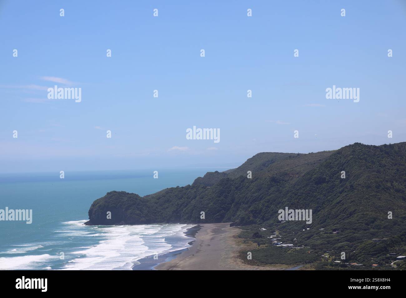 Dunkelgrüne, bewaldete Hügel, die sich über dem schwarzen Sandstrand erheben, mit sanften Meereswellen Stockfoto