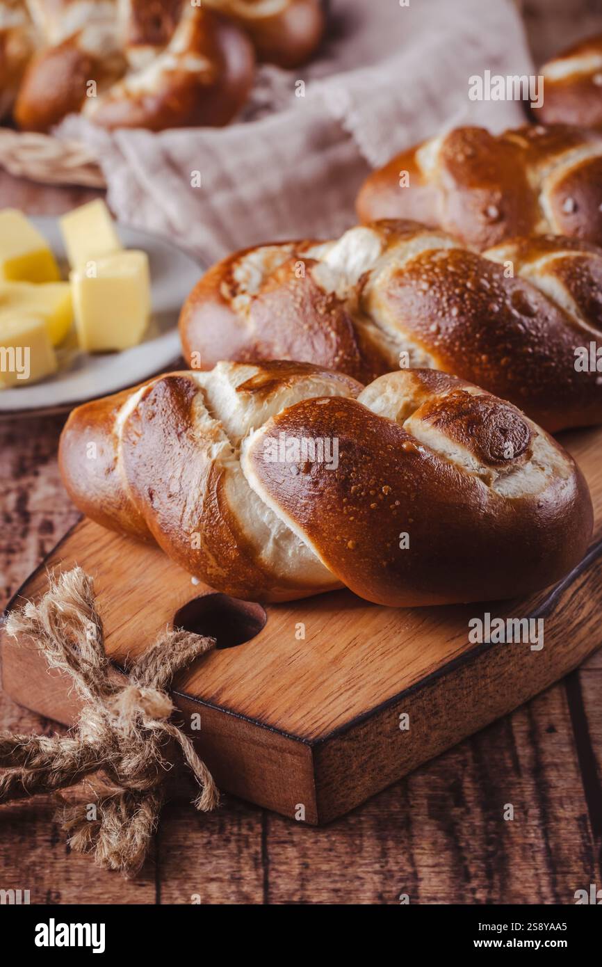 Brezelbrötchen oder Brötchen mit Butter und Salz auf hölzernem Schneidebrett Stockfoto