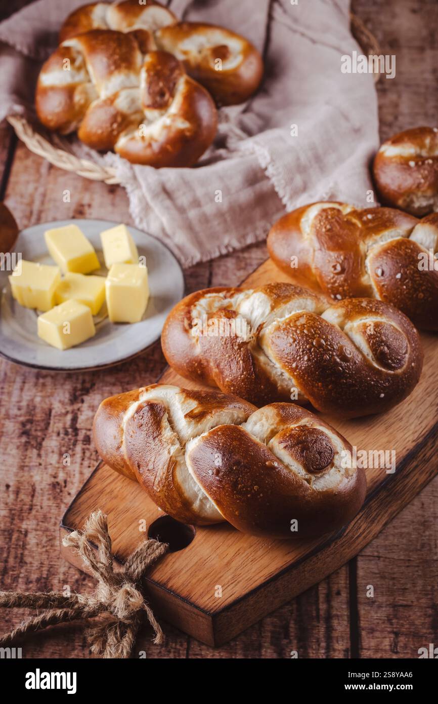 Brezelbrötchen oder Brötchen mit Butter und Salz auf hölzernem Schneidebrett Stockfoto