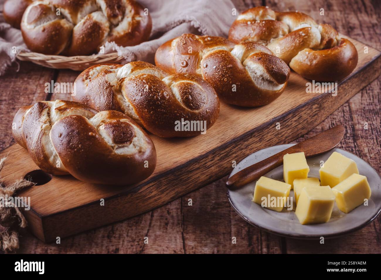 Brezelbrötchen oder Brötchen mit Butter und Salz auf hölzernem Schneidebrett Stockfoto
