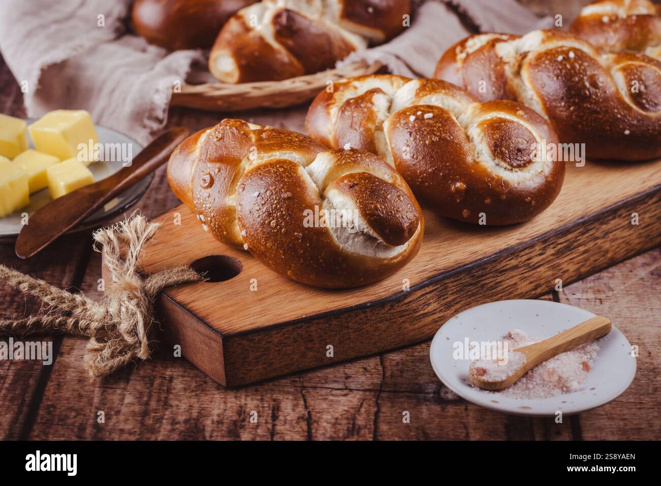 Brezelbrötchen oder Brötchen mit Butter und Salz auf hölzernem Schneidebrett Stockfoto