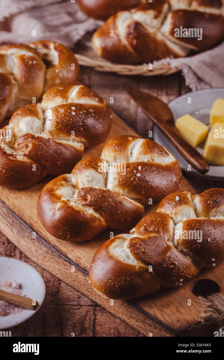 Brezelbrötchen oder Brötchen mit Butter und Salz auf hölzernem Schneidebrett Stockfoto