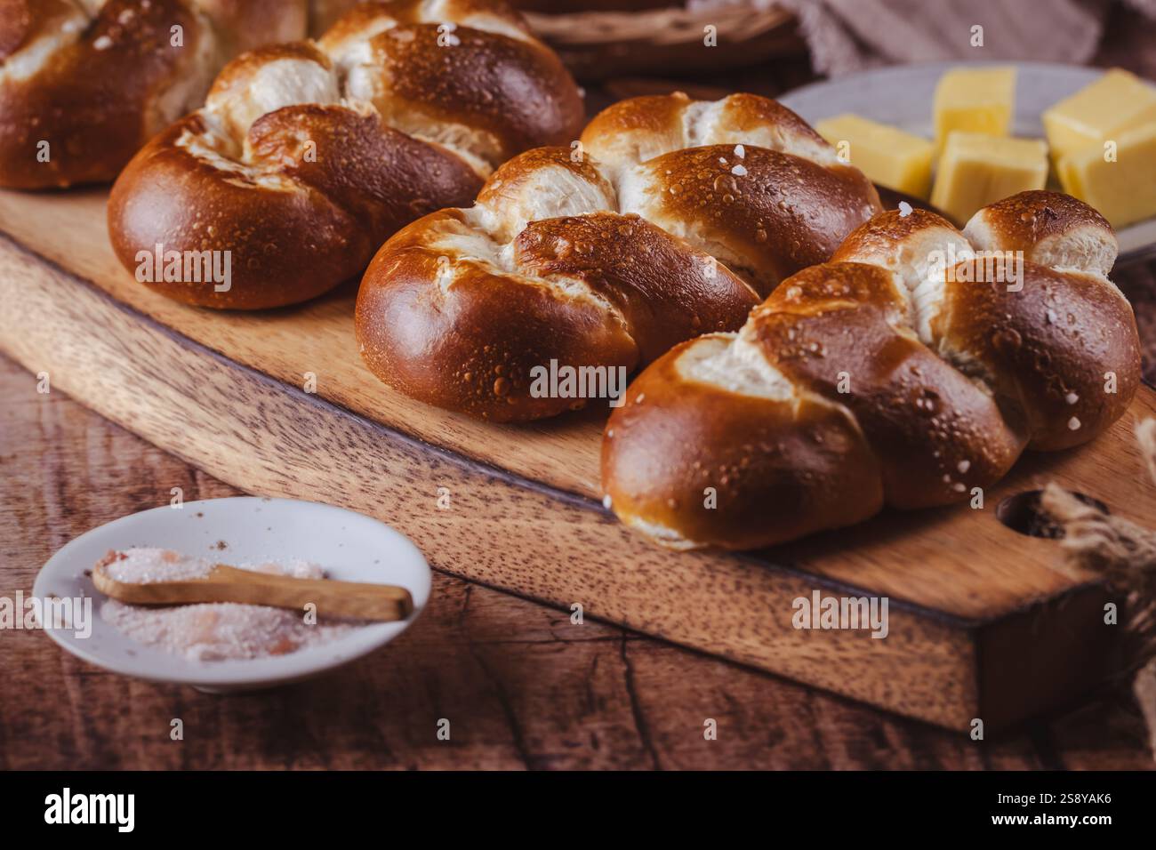 Brezelbrötchen oder Brötchen mit Butter und Salz auf hölzernem Schneidebrett Stockfoto