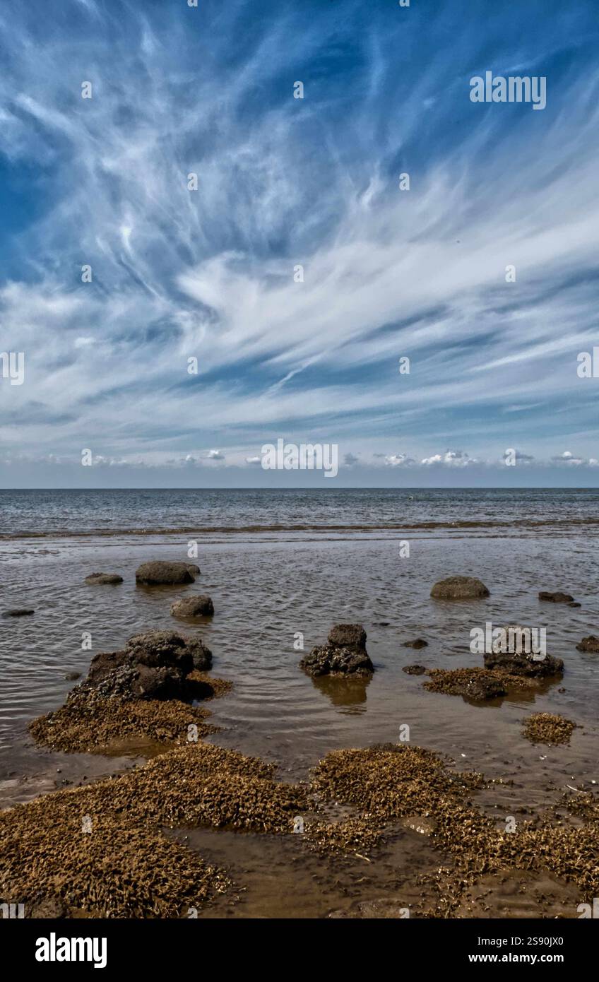 Ein englischer Strand mit Blick auf das Meer mit schrägen webby Wolkenformationen Stockfoto