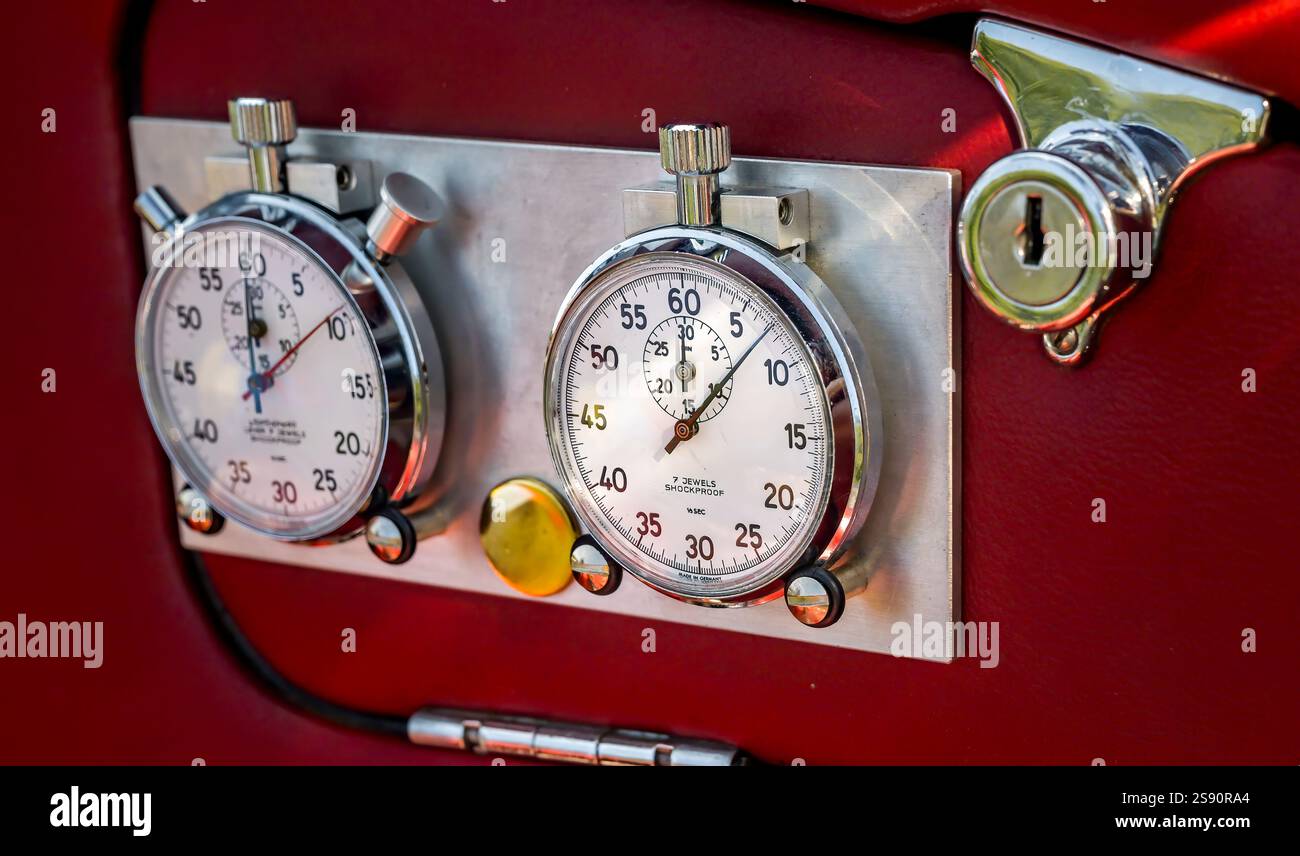 Zwei präzise Stoppuhren auf einer Metalltafel vor einem leuchtend roten Hintergrund, die das klassische Design und die Funktionalität des Automobilbaus betonen Stockfoto