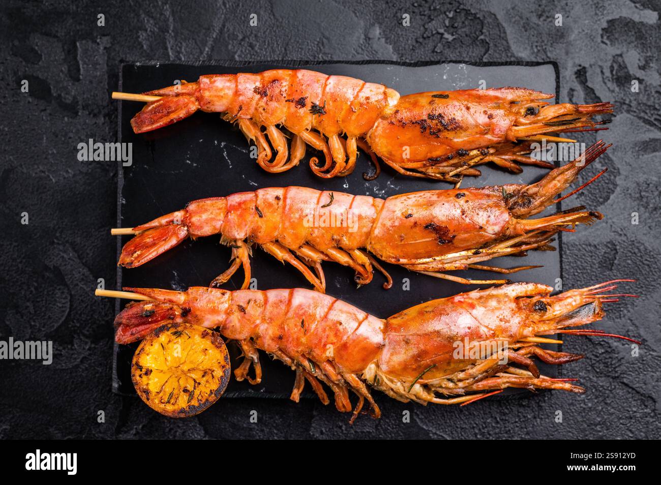 Garnelenkebab, Spieße mit gegrillten roten Garnelen Langostino Austral. Schwarzer Hintergrund. Draufsicht. Stockfoto