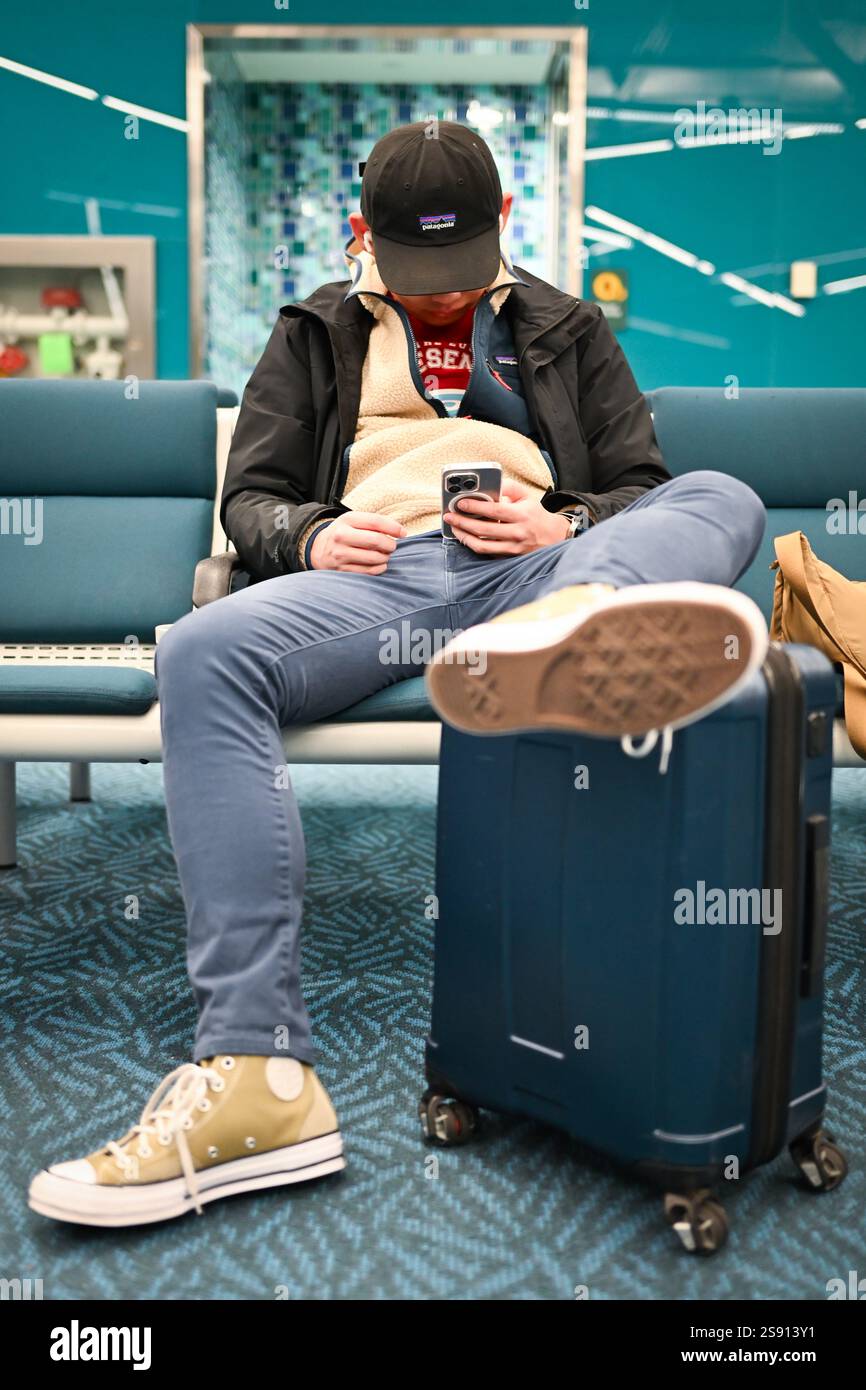 Der Mann überprüft das Telefon am Flughafen mit Fuß hoch Stockfoto