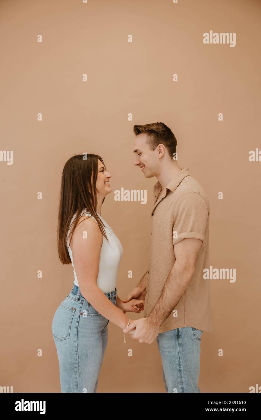 Lächelndes Paar, das zusammen vor einem beigefarbenen Studio-Hintergrund steht Stockfoto