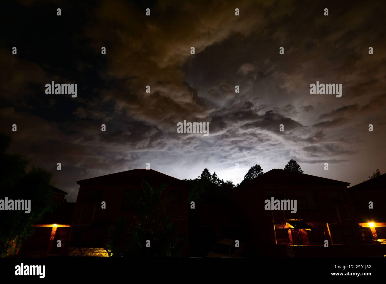 Blechbeleuchtung in Wolken hinter den Dächern städtischer Wohnhäuser. Die Natur erleuchtet den städtischen Himmel. Stockfoto