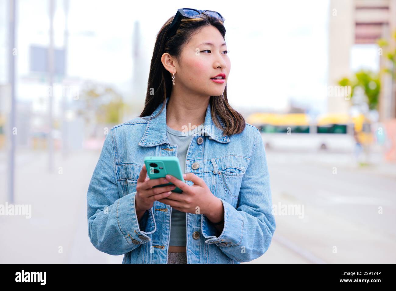 Lächelnde junge Frau, die Smartphone in der städtischen Umgebung hält Stockfoto