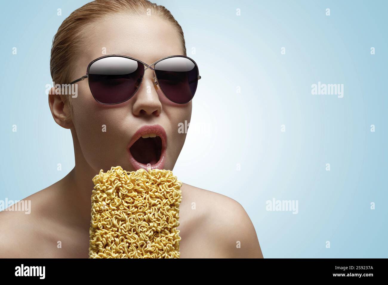 Ein kreatives Porträt eines schönen, hungrigen Mädchens, das einen Block Instant-Nudeln isst Stockfoto