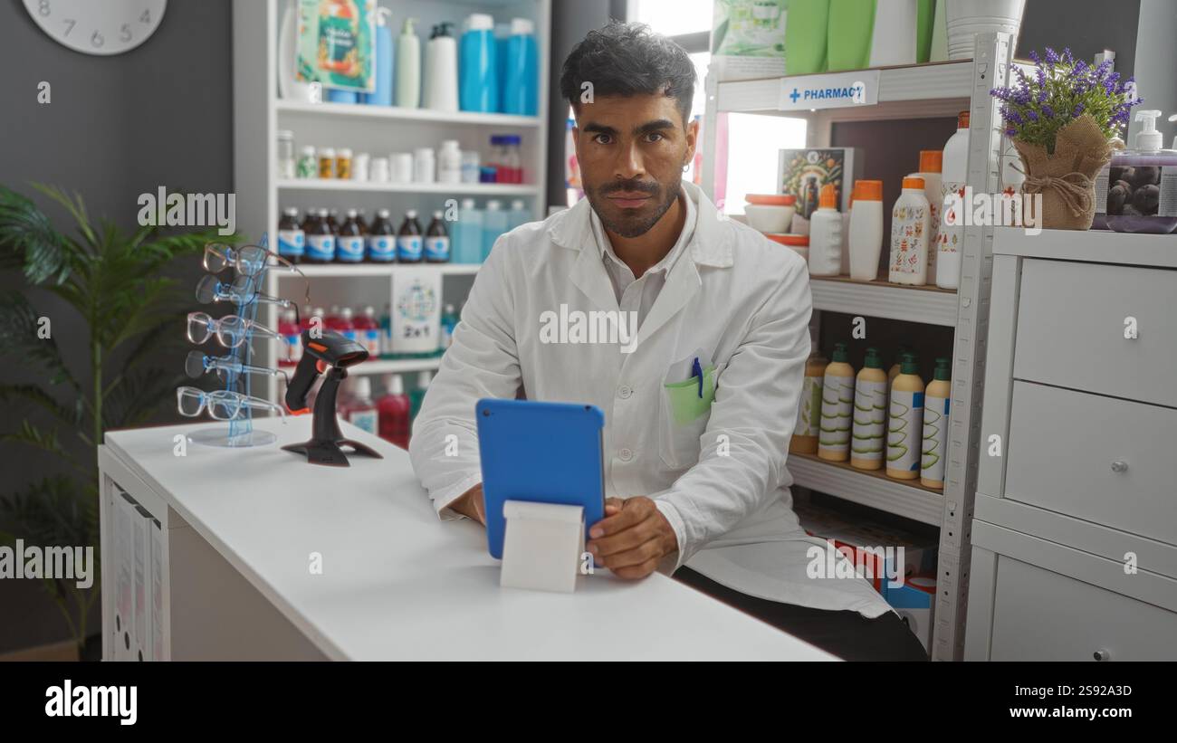 Schöner hispanischer Apotheker Mann, der Tablette in einer gut sortierten Apotheke mit Regalen für Medizin und Gesundheitsprodukte verwendet Stockfoto