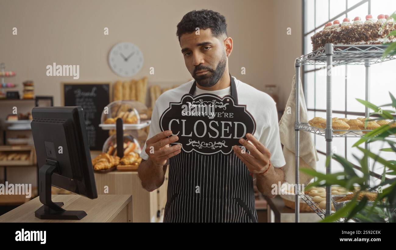 Hübscher Mann, der ein Schild in der Bäckerei hält, mit verschiedenen Backwaren und Kuchen Stockfoto