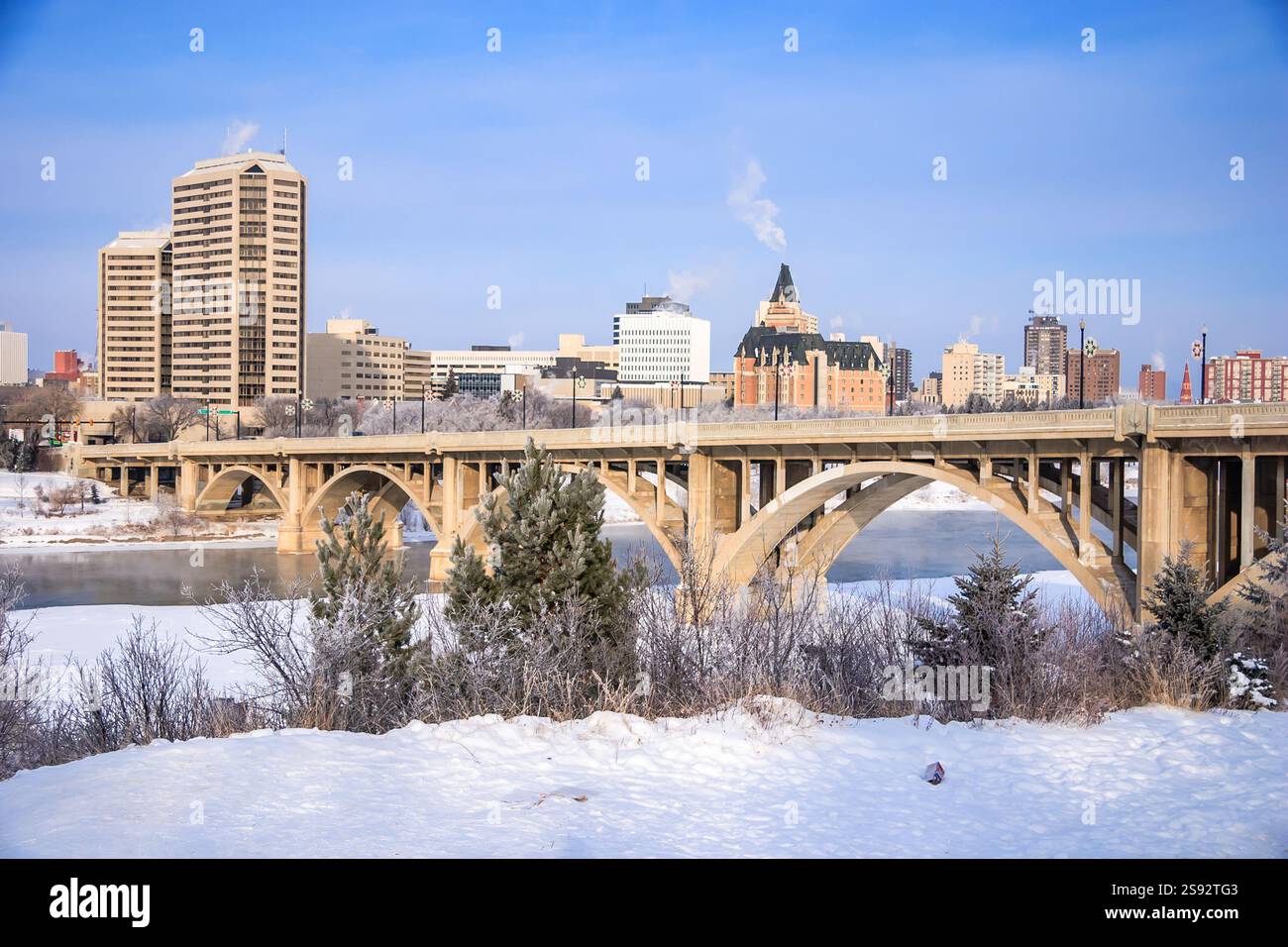 Eine Brücke über einen Fluss mit einer Stadt im Hintergrund. Der Himmel ist klar und die Sonne scheint Stockfoto