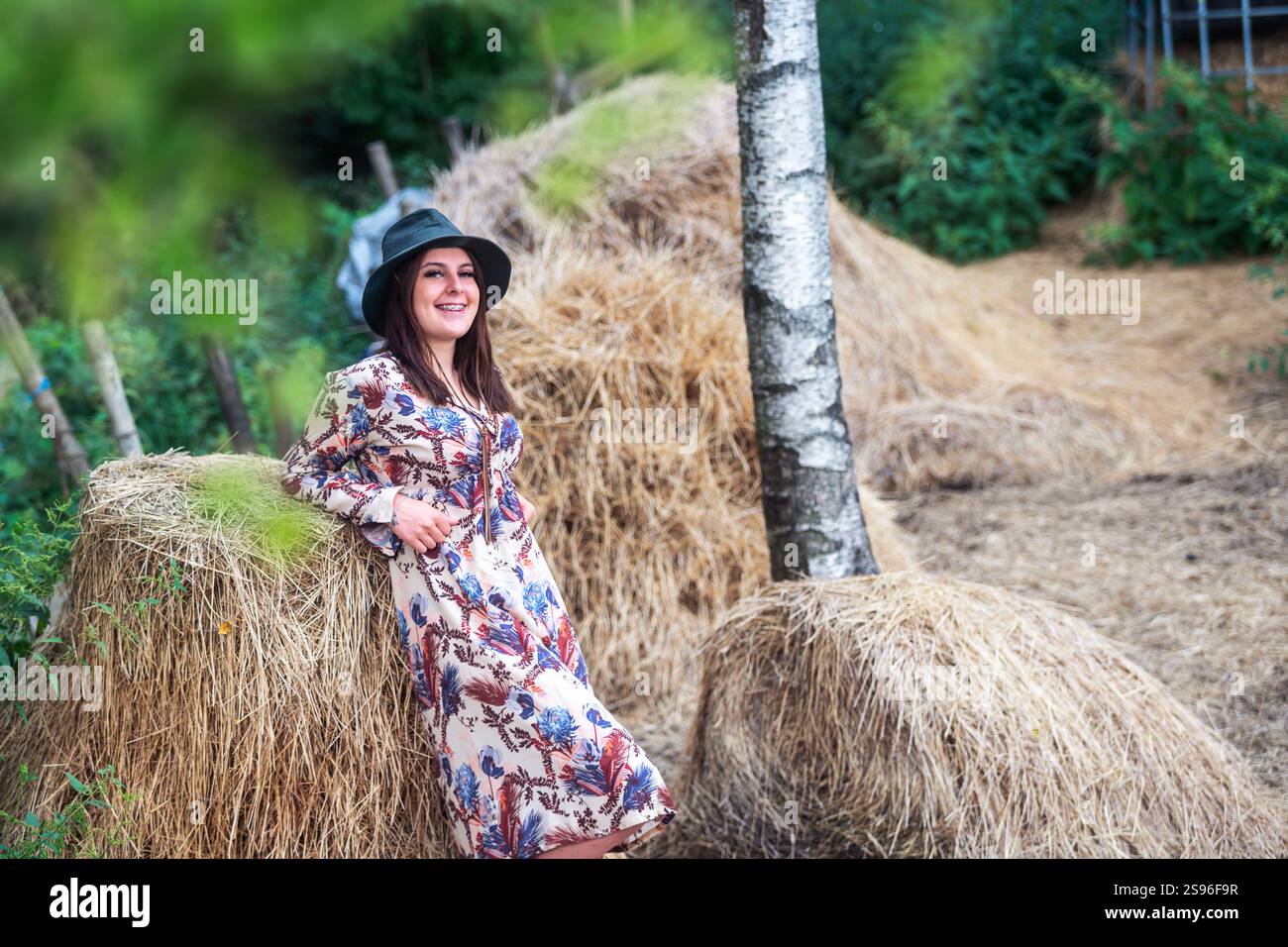 Eine elegante Frau posiert anmutig draußen in der wunderschönen Natur mit Heuballen um sich herum Stockfoto