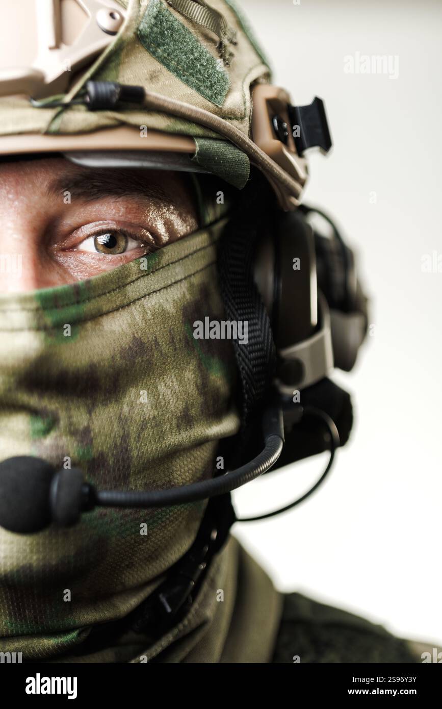 Detaillierte Ansicht des Gesichts eines Soldaten, teilweise mit taktischer Ausrüstung bedeckt, mit Tarnmustern, Kopfhörern und einem Schutzhelm, Emphas Stockfoto