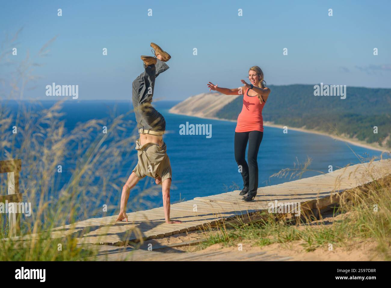 Junger erwachsener Mann, der Handstand spielt, während junge Erwachsene Frau mit nach vorne gestreckten Armen zusieht Stockfoto